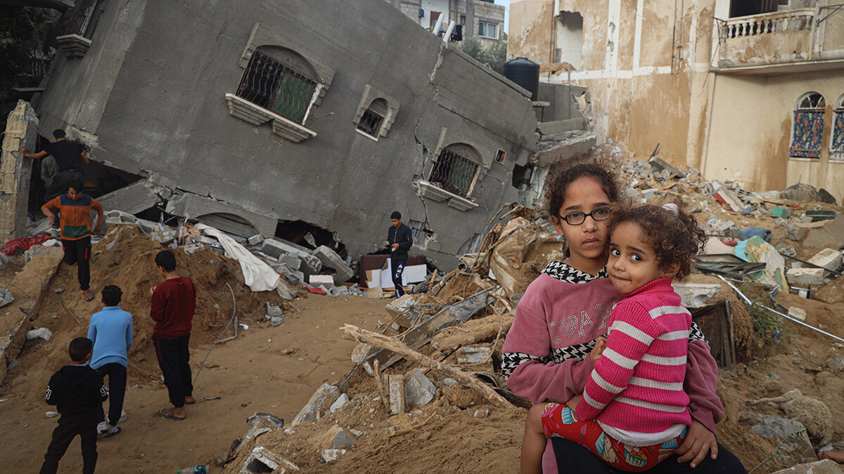 Ein junges Mädchen hält ihre Schwester vor den Trümmern ihres Hauses im Gazastreifen auf dem Arm.