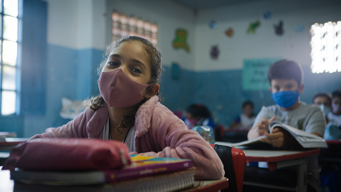 Une petite fille est assise dans une salle de classe avec un masque.