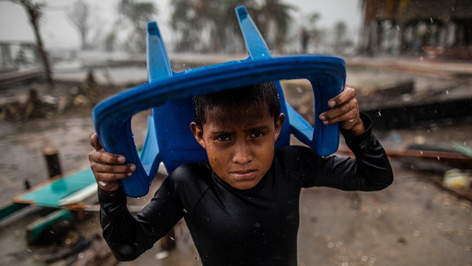 On 17 November 2020 in Bilwi, Nicaragua, a child protects himself from the heavy rain with a plastic chair, standing in the spot where his house used to be, after it was destroyed by the strong winds, swells and rains brought by Hurricane Iota.